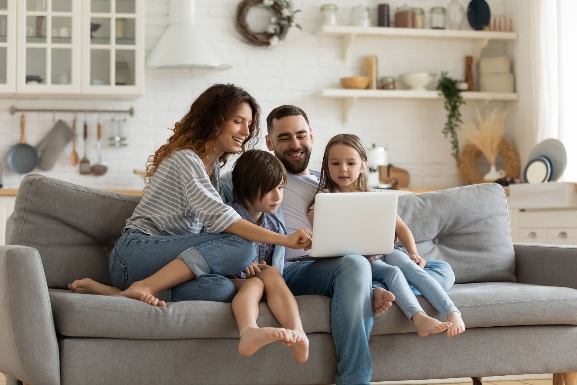 A family sits on a gray couch and crowds around a laptop.