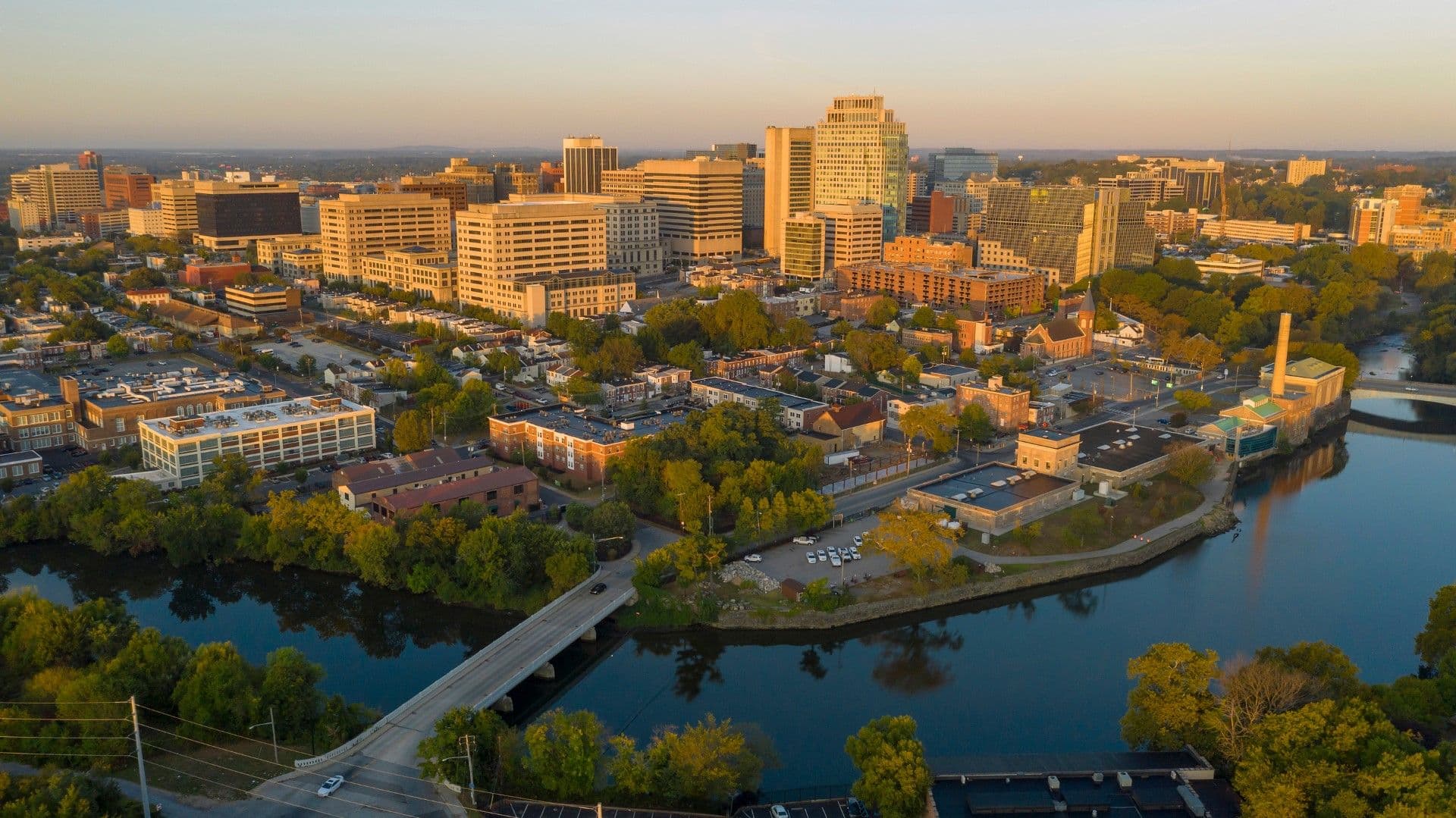 Aerial view of downtown skyline at sunset, with tall office buildings, residential areas, and the river winding through the city