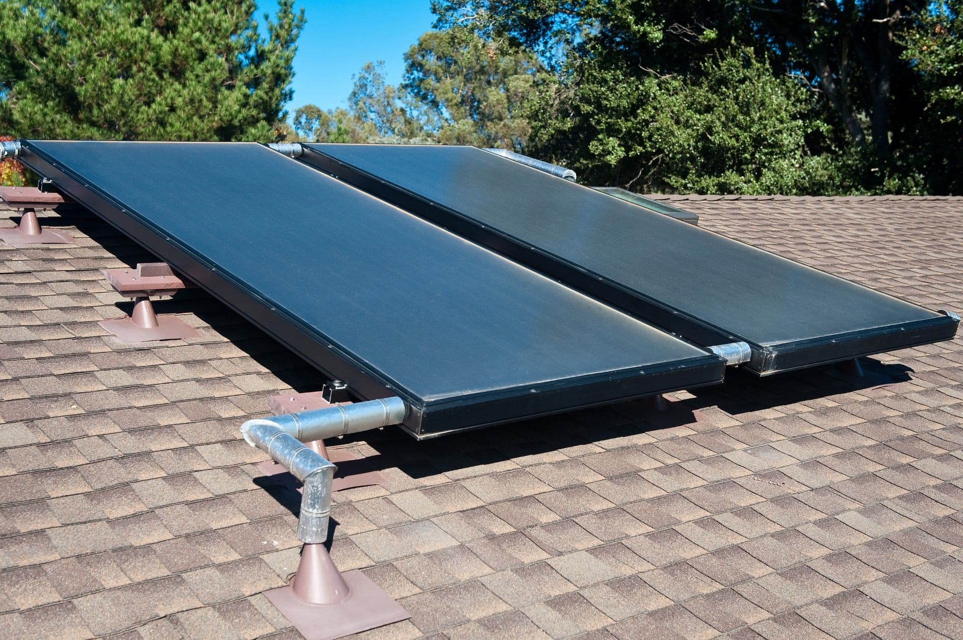 Two flat-plate solar thermal collectors mounted on a residential roof with connecting copper piping and metal supports