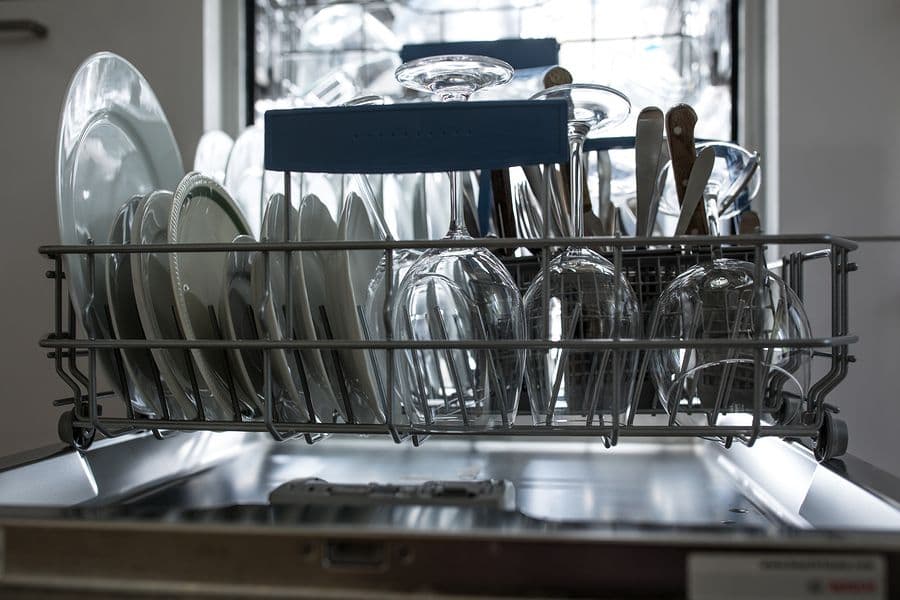 Open dishwasher with neatly arranged plates, glasses, and cutlery in a rack, showcasing an organized kitchen setting.