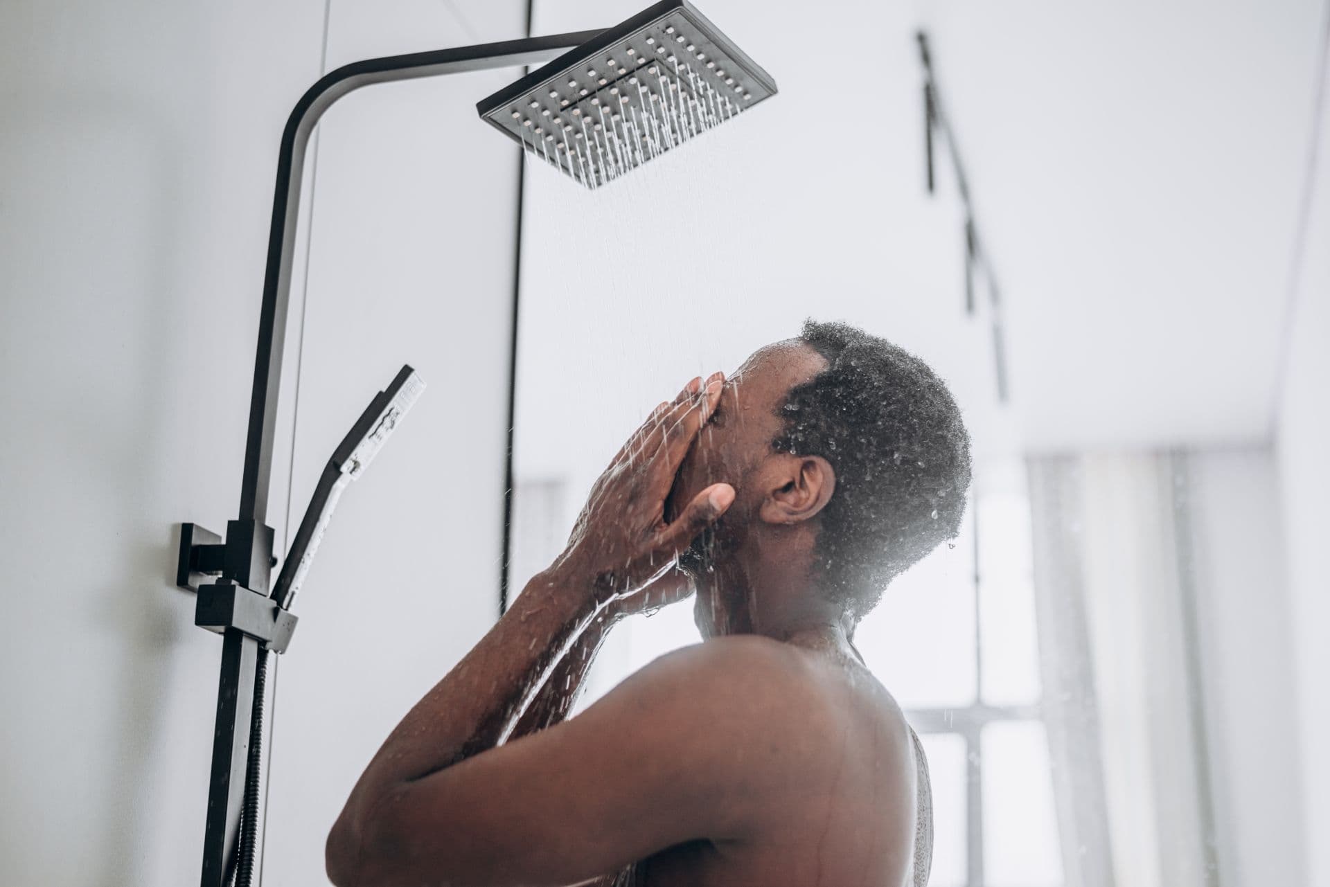 A man is positioned in front of a shower head, ready to enjoy a warm shower.